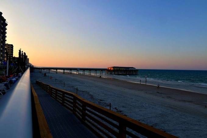 A pier stretching into the ocean at sunset, seen from a boardwalk railing.
